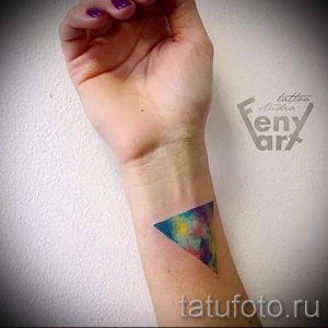 Фото тату: красочный треугольник, выполненный в технике акварели, расположен на запястье руки.