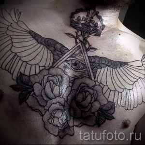 Фото тату: большая татуировка на груди, изображающая крылья, розы, корону и Всевидящее око в треугольнике. Выполнена в черно-белой гамме.