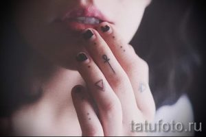 Фото тату: несколько маленьких татуировок на пальцах руки, включая треугольники и символ Анкх. Выполнено в черном цвете.