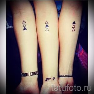 Фото тату с минималистичными треугольниками на предплечьях трех людей. Черные, серые и оранжевые треугольники расположены в ряд.