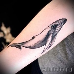 Фото тату большого кита на руке. Детализированный рисунок татуировки в стиле реализм с использованием черно-серых оттенков. Прекрасный выбор для любителей морской фауны.