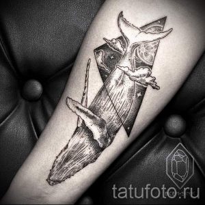 Фото тату кита, выполненного в графичном стиле с использованием геометрических фигур и точечной техники. Черно-белый рисунок татуировки на предплечье.