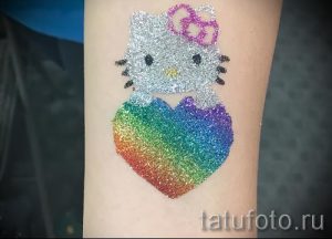 Фото тату: Hello Kitty, украшенная блестками, с радужным сердцем на руке. Идеи для ярких и позитивных временных татуировок.