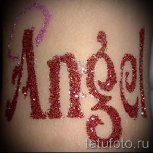 Фото тату с надписью 'Angel', выполненной блестками. Буквы красного и розового цвета расположены на коже.