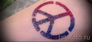 Фото тату: символ мира, выполненный из красных, синих и фиолетовых блесток на коже. Яркий и привлекательный дизайн.