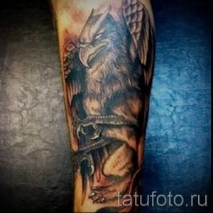 Фото тату грифона на предплечье, выполненное в реалистичном стиле. Детализированное изображение с проработкой перьев, мускулатуры и теней.