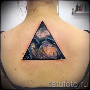 Фото тату на спине в форме треугольника, внутри которого изображена красочная галактика с закрученными спиралями и звездной пылью.