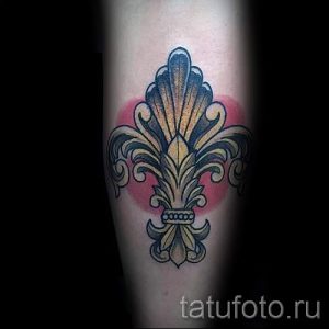 Фото тату флер-де-лис на руке. Классический рисунок татуировки выполнен в традиционном стиле с использованием черного цвета и красного фона.