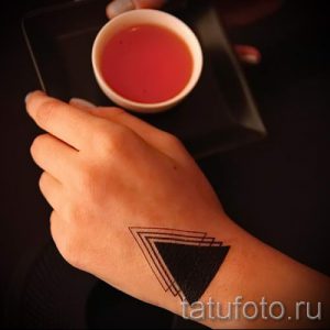Фото тату: абстрактная татуировка с изображением нескольких треугольников разного размера, расположенных друг за другом на руке, выполненная в черном цвете.