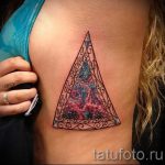 Фото татуировки на боку: треугольник с космическим фоном и надписью 'We are all stardust'. Детализированный рисунок, темные тона.