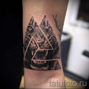 Фото тату на предплечье: голова волка, разделенная геометрическими треугольниками. Детализированный рисунок татуировки в черно-белых тонах.