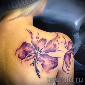 Фото тату акварельной лилии в фиолетовых и розовых тонах, расположенной на плече девушки.