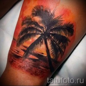Фото тату: татуировка пальмы на фоне заката на предплечье. Реалистичное изображение с использованием теплых цветов.