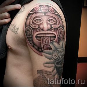 Фото тату маски ацтеков на плече. Черно-серые тона, детализированная проработка, этнический стиль.
