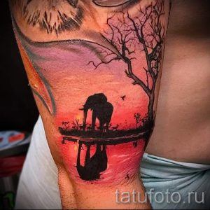 Фото тату реалистичного слона, стоящего у воды на фоне заката. Детализированный рисунок татуировки с отражением в воде.