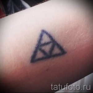 Фото тату: простой черный треугольник на внутренней стороне предплечья. Минималистичный рисунок татуировки, выполненный тонкими линиями.