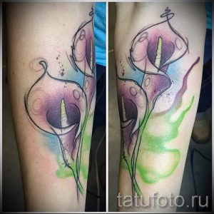 Фото тату двух калл в акварельном стиле на руке. Нежные переходы цветов, размытые контуры и легкий эффект брызг.