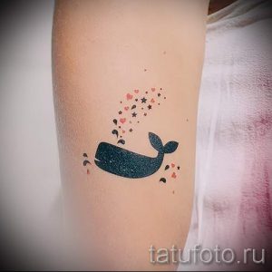 Фото милой татуировки кита, окруженного сердечками и звездами на руке. Черно-белый рисунок с нежными деталями.