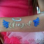 Фото временной татуировки: надпись "Angel" золотыми блестками, с голубыми крыльями и серебряным нимбом. Идеально для детских праздников и вечеринок.