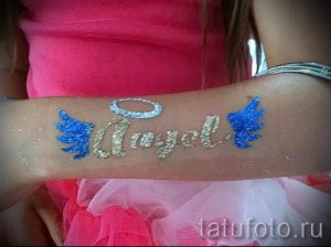 Фото временной татуировки: надпись "Angel" золотыми блестками, с голубыми крыльями и серебряным нимбом. Идеально для детских праздников и вечеринок.