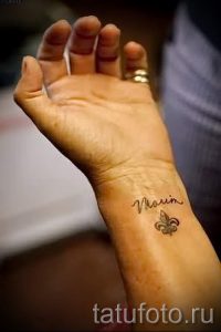 Фото тату с надписью "Morin" и изображением флер-де-лис на запястье. Минималистичный дизайн в черном цвете.