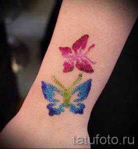 Фото тату с изображением двух разноцветных бабочек, выполненных блестками на коже. Идеально для вдохновения и поиска идей для временных татуировок.