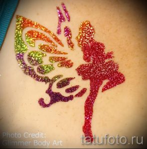 Фото тату с изображением феи, выполненной блестками на коже. Крылья феи выполнены в радужных цветах.