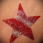 Фото тату: яркая красная звезда, выполненная блестками, на коже. Простой, но эффектный дизайн, привлекающий внимание.