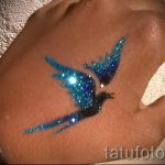 Фотография татуировки в виде птицы, выполненной голубыми блестками на руке. Динамичный и привлекательный рисунок.