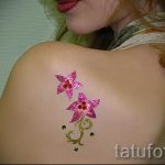Фотография татуировки в виде двух звезд и стебля с листьями, выполненной розовыми блестками на плече. Нежный и привлекательный рисунок.