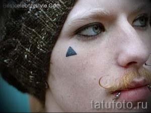 Фото тату: небольшой черный треугольник под глазом. Минималистичный и необычный дизайн, привлекающий внимание.