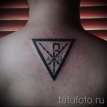 Фото тату на спине: минималистичный рисунок в виде черного треугольника с символами Альфа и Омега внутри. Простой и стильный эскиз татуировки.
