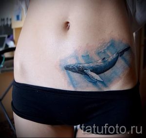 Фото акварельной тату кита на женском животе. Нежный рисунок татуировки с плавными переходами цветов и эффектом размытости.