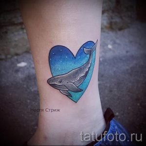 Фото тату кита, плывущего внутри сердца, на лодыжке. Нежные голубые и синие оттенки создают романтичное настроение.