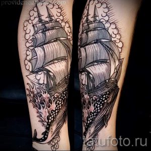 Фото тату парусника в стиле олд скул на икре. Детализированный рисунок корабля, волн и облаков, выполненный в черных тонах.