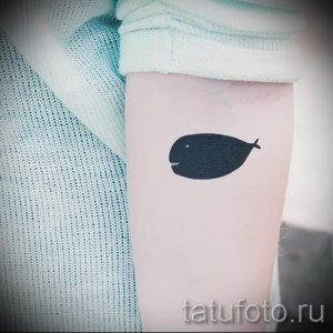 Фото минималистичной татуировки кита на ноге. Простой черный силуэт кита, выполненный в лаконичном стиле.