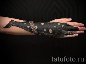 Фото тату кита на руке, выполненное в технике дотворк. Черный рисунок с точками и линиями, создающий эффект градиента.
