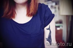 Фото тату: небольшая, изящная татуировка хвоста кита на руке, выполненная в черно-белой графике с тонкими линиями.