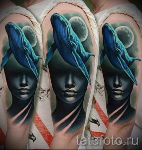 Фото тату: впечатляющая татуировка на плече, изображающая кита, выплывающего из женского лица, выполненная в реалистичной технике с использованием серых и голубых оттенков.