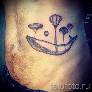 Черно-белое фото тату кита на боку. Кит парит в воздухе, к которому привязаны воздушные шары разных форм.