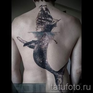 Фото большой татуировки кита, плывущего под парусным кораблем, на мужской спине. Детализированный черно-белый рисунок татуировки.