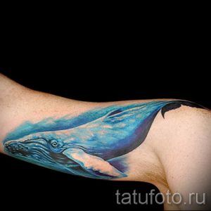 Фото тату: Акварельная татуировка кита на руке, выполненная в синих и голубых тонах. Размытые контуры и плавные переходы цвета.