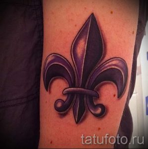 Фото тату флер-де-лис на предплечье, выполненное в черно-серых тонах с использованием теней для создания объема. Классический символ геральдики.