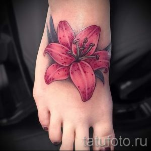 Цветное фото тату лилии на женской стопе. Красивый рисунок татуировки с реалистичной проработкой лепестков и листьев.
