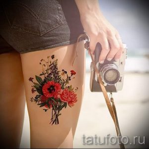 Фото тату букета маков и других цветов на бедре. Красные маки, зеленые листья и яркие цветы создают красивый рисунок.