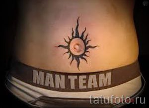 Фото тату солнца с надписью 'Man Team' на животе мужчины. Оригинальный рисунок татуировки в черных тонах.