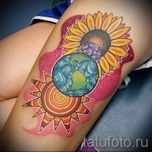 Фото тату: Композиция из солнца, Земли и цветка на бедре. Яркий и красочный рисунок татуировки, выполненный в стиле акварель.