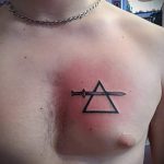 Фото тату: Черный треугольник с мечом, пронзающим его, на груди мужчины. Символическая татуировка с элементами графики.