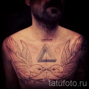 Фото тату: Татуировка на груди мужчины с треугольником, птицами и надписью. Рисунок выполнен в графическом стиле.
