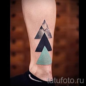 Фото татуировки на икре, состоящей из четырех геометрических фигур - треугольников, выполненных в разных цветах: сером, черном и мятном.